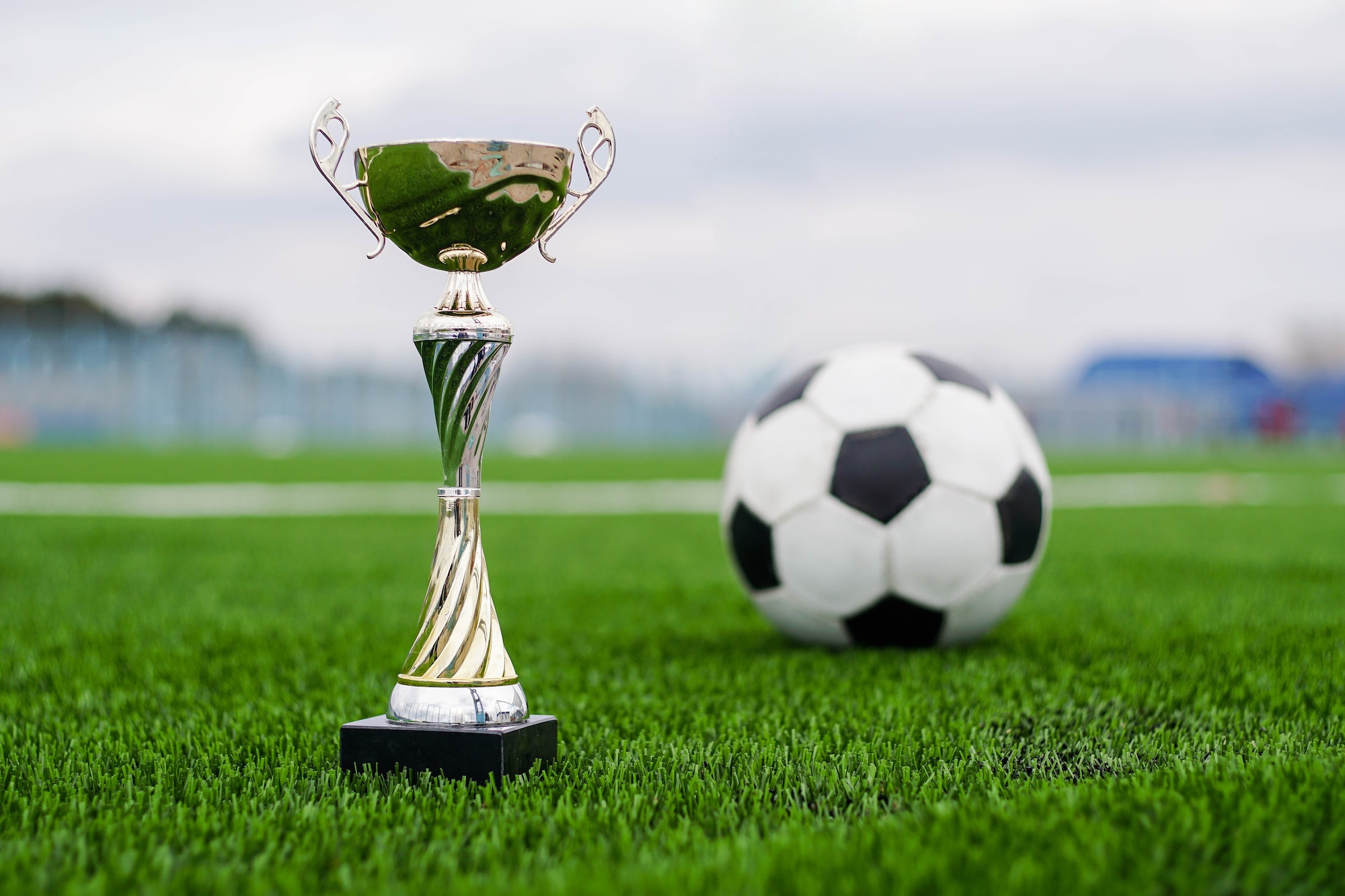 Golden football cup with soccer ball on field.