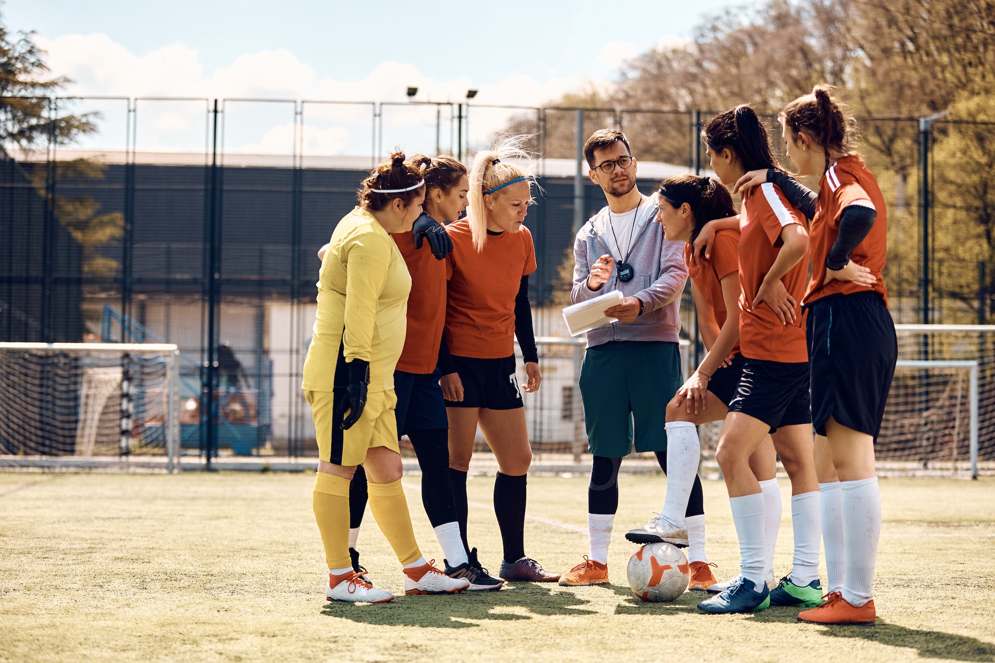 Soccer coach planning game strategy with female team on playing field.